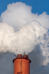  Clouds of smoke ascend from the pipes of an industrial enterprise against a blue sky
