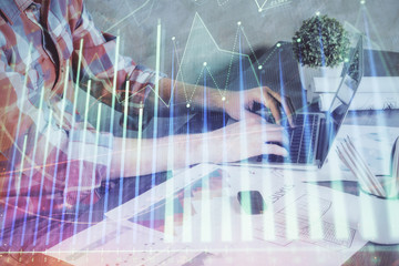 Double exposure of stock graph with businessman typing on computer in office on background. Concept of hard work.