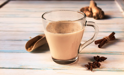 Hot healthy indian masala chai or tea with diferent spices (cardamon, anice, cinnamon, ginger) on a white wooden background
