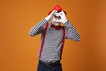Fototapeta na wymiar Mime in vest and red hat with heart made of palms on orange background