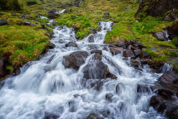 Beautiful nature landscape with flowing water of the fast stream through the green summer valley, outdoor natural background, Iceland