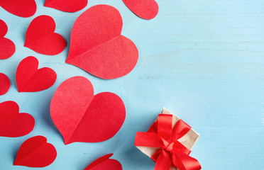 Red hearts cut out of paper and a small gift box on a blue background.