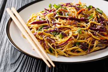 Stir-fried egg noodles with red cabbage, carrots, herbs and sesame seeds close-up in a plate. horizontal