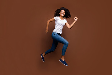 Fototapeta na wymiar Full length profile photo of funny dark skin lady jumping high rushing mall black friday shopping addicted wear casual white t-shirt jeans isolated brown color background