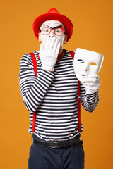 Surprised mime in red hat and in vest with white mask on orange background