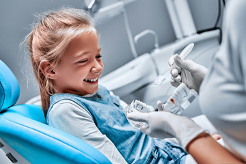 The dentist tells the child about oral hygiene and shows an artificial jaw and toothbrush - obrazy, fototapety, plakaty