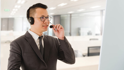 Portrait of Asian smiling businessman customer support phone operator in office space background and copy space.Concept call center job and telemarketing service.