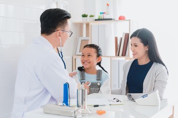 Professional doctor wearing white coat using stethoscope to examine kid patient with her mother in hospital background.Concept of disease treatment and health care in hospitals.