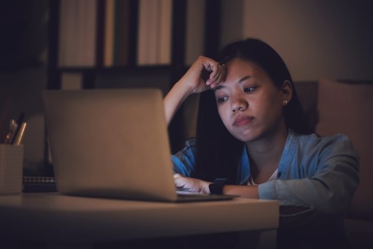 Asian woman student or businesswoman work late at night. Concentrated and feel sleepy at the desk in dark room with laptop or notebook.Concept of people workhard and burnout syndrome.