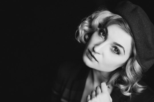 Beautiful blonde woman in a beret looks at the camera in retro style black and white photo. Close-up portrait. Soft focus.