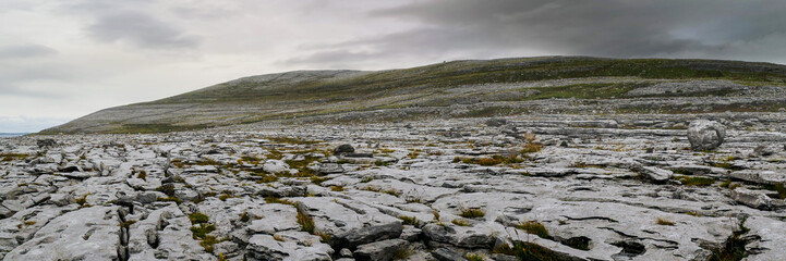 Panorama image of Burren landscape, county Clare, Ireland, Rough stone terrain, Cloudy sky.