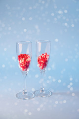 Two champagne glasses with red heart shaped sugar candy. Over blue background. Valentines Day, anniversary or wedding celebration concept.  Copy space.