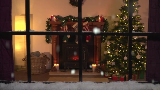 4K: Window Scene at Christmas. Looking into home with snow falling outside. Christmas Tree and fireplace in lounge