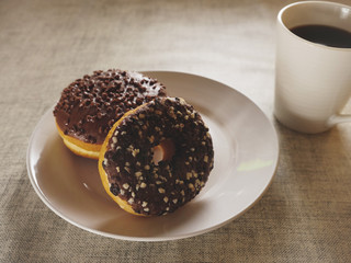 Two chocolate doughnut on a white plate and a cup of tea on a simple table cloth, Concept break, breakfast.