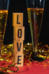 Two sparkling champagne glasses, with gold confetti and red background with wooden pieces with the message love.