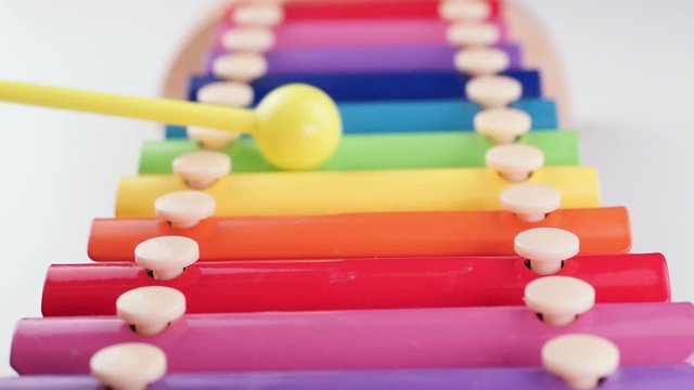 A child plays on a children xylophone painted with rainbow colors on a white background. Close-up