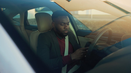 Los Angeles, California 15/03/2019 EDITORIAL: Smiling attractive african american young businessman use phone in a car sits behind the wheel young smile vehicle open passenger arm auto street
