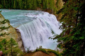 Beautiful wild waterfall on turquoise river. Steep slopes covered with trees. Rocky Mountains, Canada.