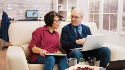 Elderly age couple using laptop while sitting on sofa