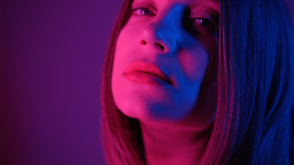 Side footage of stunning young woman with bob hairstyle turning around and looking directly at camera. Makeup, model. Seductive look. Close-up shooting. Neon lighting, studio.