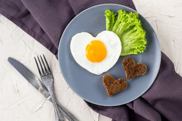 Valentines day breakfast with heart shaped fried eggs served on grey plate