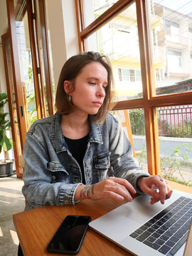 Young funny tattooed freelance girl texting mesage on her phone and drinking coffee