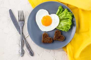 Valentines day breakfast with heart shaped fried eggs served on grey plate and yellow napkin