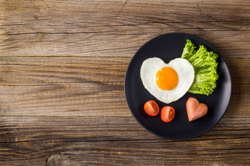 Fried eggs in the shape of a heart with sausages, herbs and tomatoes. Breakfast on Valentine's day on white background