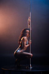 attractive stripper in underwear sitting near pole on blue and orange