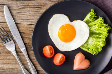 Valentines day breakfast with heart shaped fried eggs served on grey plate.