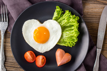 Valentines day breakfast with heart shaped fried eggs served on grey plate.