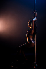 side view of stripper in fishnet tights dancing striptease near pylon on black