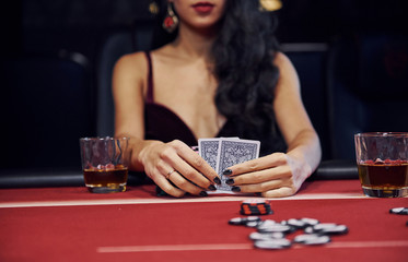 Woman in elegant clothes sits in cassino by table and plays poker game - obrazy, fototapety, plakaty