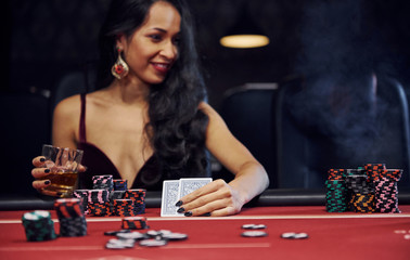 Fototapeta premium Woman in elegant clothes sits in cassino by table and plays poker game