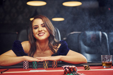 Woman in elegant clothes sits in cassino by table and plays poker game - obrazy, fototapety, plakaty