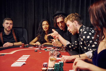With glasses of drink. Group of elegant young people that playing poker in casino together