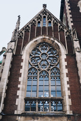 Catholic church. Baroque and Gothic architecture. Vaulted round window with stained glass on facade of the building.