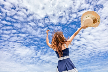 Happy Woman in summer vacation holding hat and wearing dress enjoying the view at the island beach.