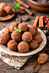 Pile of homemade chocolate truffles rolled in cocoa powder on plate on a wooden table. Tasty sweet dessert. Raw chocolate truffles, vegan chocolate