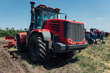 Fototapeta premium red tractor with big wheels in the field against the blue sky