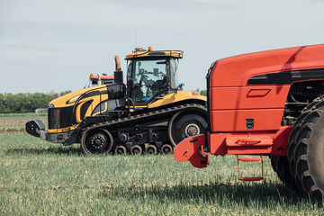 Obraz premium żółta gąsienica i czerwony traktor z dużymi kołami w polu przeciw błękitne niebo