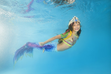 A girl in a mermaid costume poses underwater in a pool. Young beautiful girl poses underwater in...