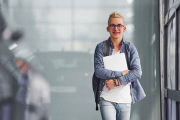 Young hipster guy in nice clothes stands indoors against grey background and near car