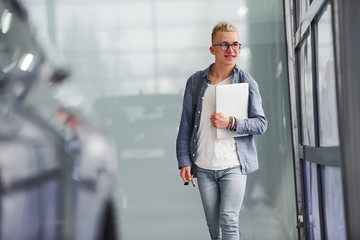 Young hipster guy in nice clothes stands indoors against grey background and near car