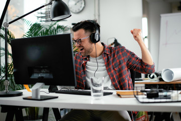 Attractive businessman in office. Young programmer with headphones singing at work. 
