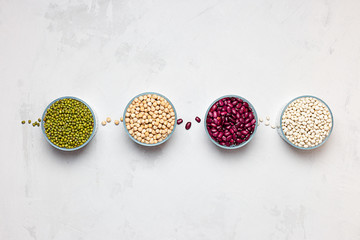 Bowls of various legumes: chickpeas, lentils, mung, red and white bean on a white background.