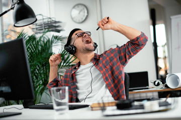 Attractive businessman in office. Young programmer with headphones singing at work. 