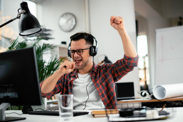 Attractive businessman in office. Young programmer with headphones singing at work. 