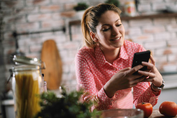 Young beautiful woman in kitchen using smartphone. Portrait of pretty woman in kitchen. 