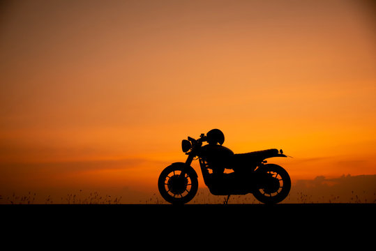 Silhouette of motorcycle parking with sunset background in Thailand, Young Traveller man placed helmet on motorbike. Trip and lifestyle of Motorcycle Concept